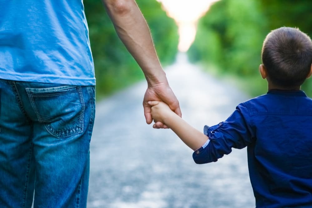 Father is Holding hand of his child and walking on road